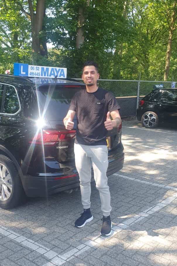 Een leerling met twee duimen omhoog naast de lesauto