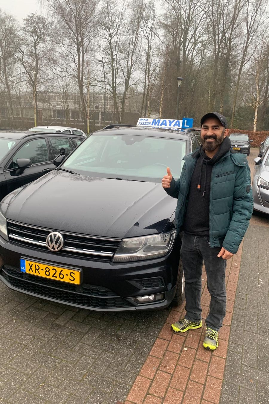 Een leerling steekt zijn duim op naast de zwarte lesauto van Verkeersschool Maya