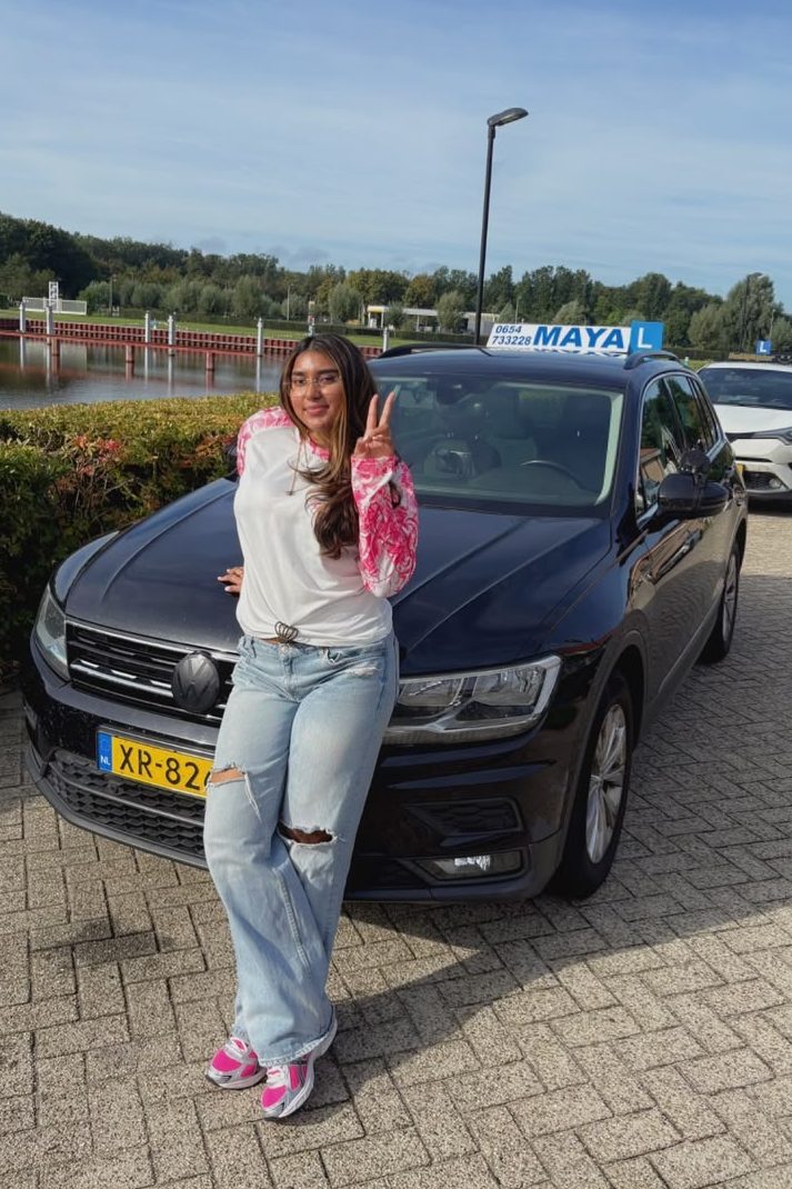 Een leerling leunt lachend tegen de lesauto met het MAYA-daklicht