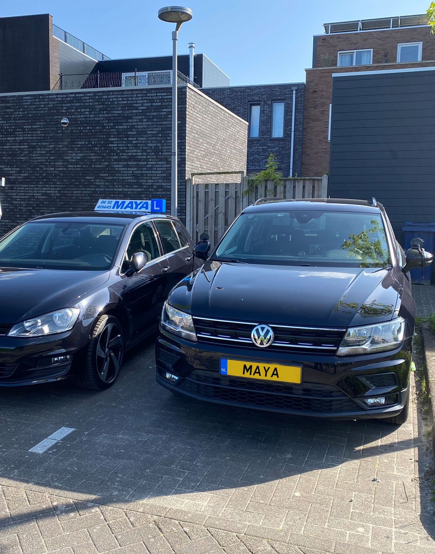 De twee zwarte lesauto's van Verkeersschool Maya, een met het witte MAYA-daklicht en een met het gele kenteken MAYA